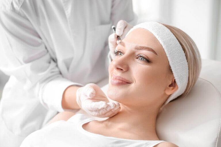 young women receiving eyebrow correction treatment in a beauty salon, showing a Professional applying the procedure.