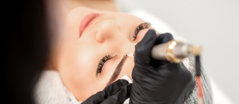 Permanent makeup artist performing eyebrow tattooing with precision tool