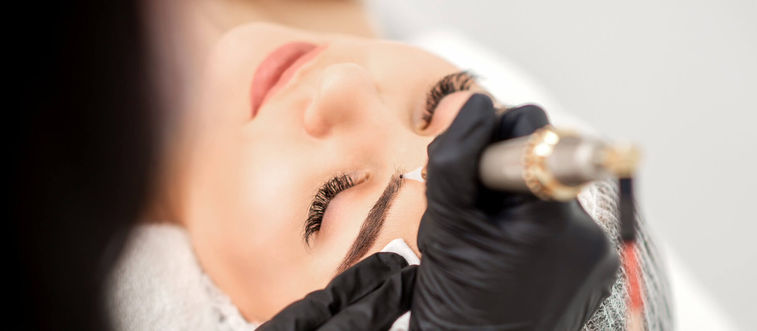 Permanent makeup artist performing eyebrow tattooing with precision tool